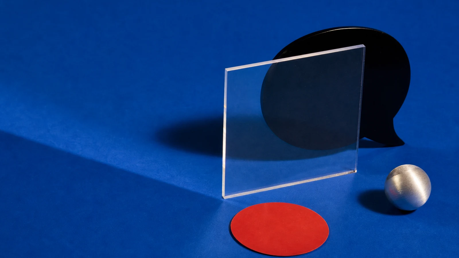Escultura negra con forma de diálogo, placa transparente, esfera metálica, y círculo rojo sobre fondo azul